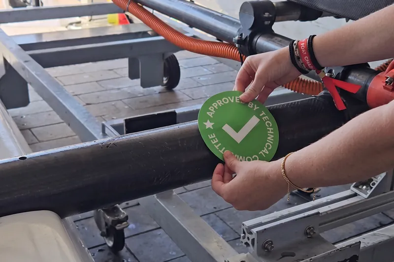 Two hands applying a green technical-committee approval sticker to the boat frame.