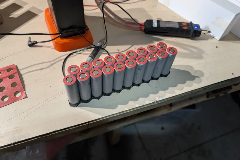 Nineteen cylindrical 21700 cells with red insulating rings standing in a staggered holder on the bench.