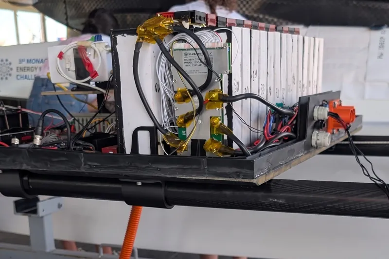 The white PCM-CAGE pack with its battery management board and copper connectors, mounted on the carbon frame of the catamaran.